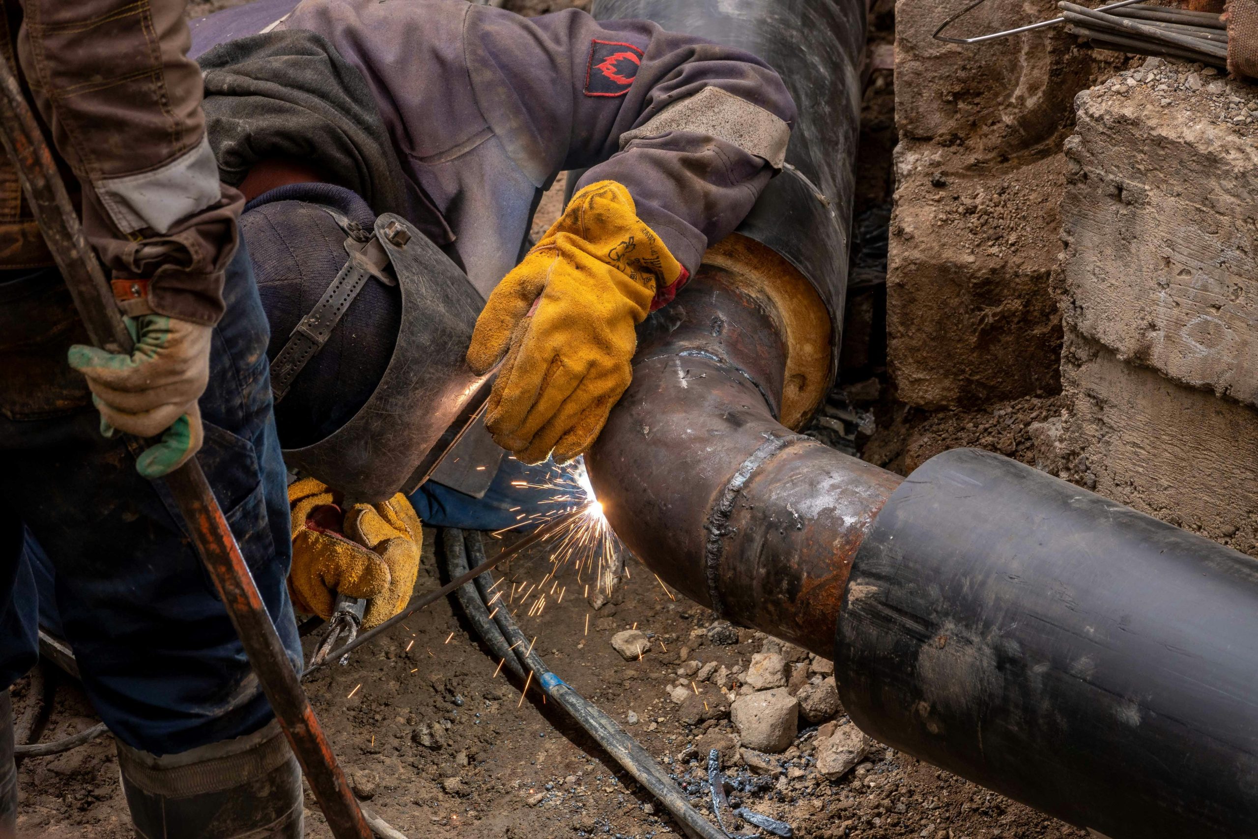Close-up of a skilled worker welding a steel pipe outdoors at a construction site.